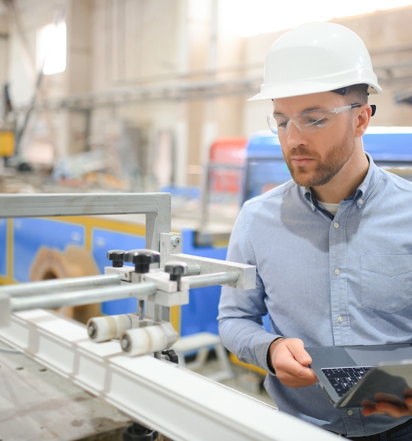 Engineer in hardhat is using a laptop in a heavy industry factory